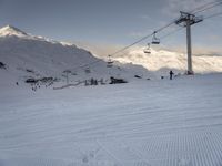 skiers ride up a snowy slope in the mountains with a sky lift overhead above