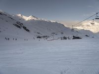 skiers ride up a snowy slope in the mountains with a sky lift overhead above