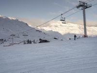 skiers ride up a snowy slope in the mountains with a sky lift overhead above