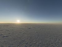 the sun shines on the vast open desert plains at sunset time, and there are footprints in the snow