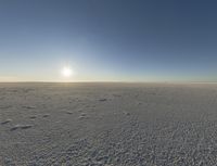 the sun shines on the vast open desert plains at sunset time, and there are footprints in the snow