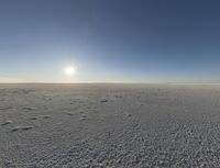 the sun shines on the vast open desert plains at sunset time, and there are footprints in the snow