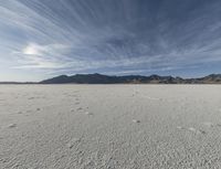 a plain with tracks left in the sand on it's horizon, and mountains in the background