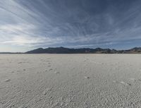 a plain with tracks left in the sand on it's horizon, and mountains in the background