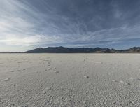 a plain with tracks left in the sand on it's horizon, and mountains in the background