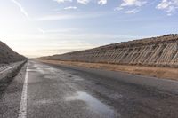 a paved highway surrounded by a sandy hillside area and a desert with no vehicles driving on it