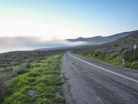 a motorcycle driving down a rural country road on a clear day with fog in the distance