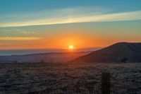 there is a sunset in the horizon on a field with grassy land below the mountains