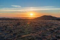 there is a sunset in the horizon on a field with grassy land below the mountains