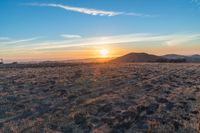 there is a sunset in the horizon on a field with grassy land below the mountains