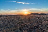 there is a sunset in the horizon on a field with grassy land below the mountains