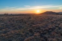 there is a sunset in the horizon on a field with grassy land below the mountains