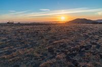 there is a sunset in the horizon on a field with grassy land below the mountains