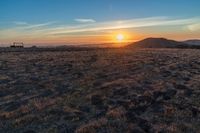 there is a sunset in the horizon on a field with grassy land below the mountains