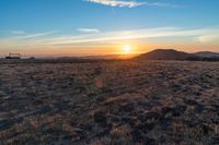 there is a sunset in the horizon on a field with grassy land below the mountains