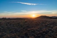 there is a sunset in the horizon on a field with grassy land below the mountains