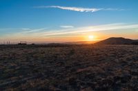 there is a sunset in the horizon on a field with grassy land below the mountains