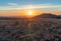 there is a sunset in the horizon on a field with grassy land below the mountains