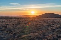 there is a sunset in the horizon on a field with grassy land below the mountains