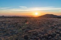 there is a sunset in the horizon on a field with grassy land below the mountains