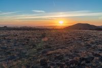 there is a sunset in the horizon on a field with grassy land below the mountains