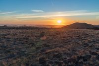 there is a sunset in the horizon on a field with grassy land below the mountains