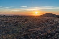 there is a sunset in the horizon on a field with grassy land below the mountains