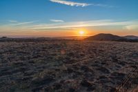 there is a sunset in the horizon on a field with grassy land below the mountains