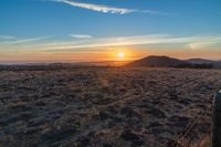 there is a sunset in the horizon on a field with grassy land below the mountains