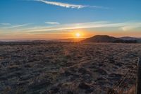 there is a sunset in the horizon on a field with grassy land below the mountains