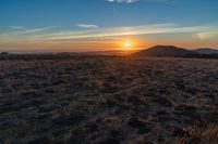 there is a sunset in the horizon on a field with grassy land below the mountains