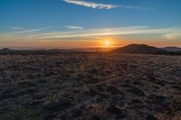 there is a sunset in the horizon on a field with grassy land below the mountains