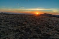 there is a sunset in the horizon on a field with grassy land below the mountains