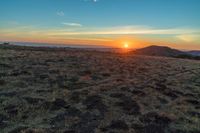 there is a sunset in the horizon on a field with grassy land below the mountains