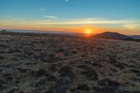 there is a sunset in the horizon on a field with grassy land below the mountains