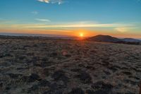 there is a sunset in the horizon on a field with grassy land below the mountains