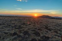 there is a sunset in the horizon on a field with grassy land below the mountains