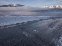 there is some ice on the road next to mountains with snow and clouds covering them