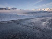 there is some ice on the road next to mountains with snow and clouds covering them