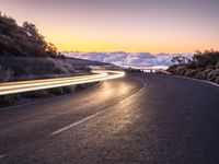 an empty winding road on a mountain with the sun set above the mountains in the background