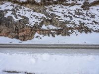 a person walking down the snow on a mountain road, next to rocks and snow