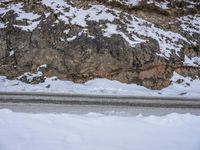 a person walking down the snow on a mountain road, next to rocks and snow