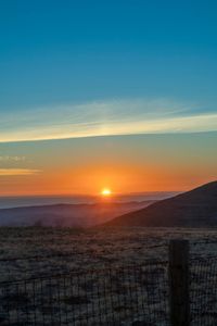 there is a sunset in the horizon on a field with grassy land below the mountains