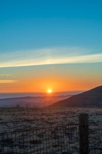 there is a sunset in the horizon on a field with grassy land below the mountains