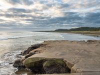 rocks next to the water in the middle of the beach and waves coming ashore on the shore