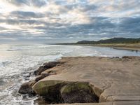 rocks next to the water in the middle of the beach and waves coming ashore on the shore