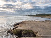 rocks next to the water in the middle of the beach and waves coming ashore on the shore