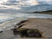 rocks next to the water in the middle of the beach and waves coming ashore on the shore