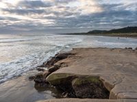 rocks next to the water in the middle of the beach and waves coming ashore on the shore