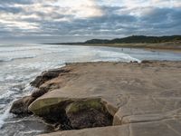 rocks next to the water in the middle of the beach and waves coming ashore on the shore